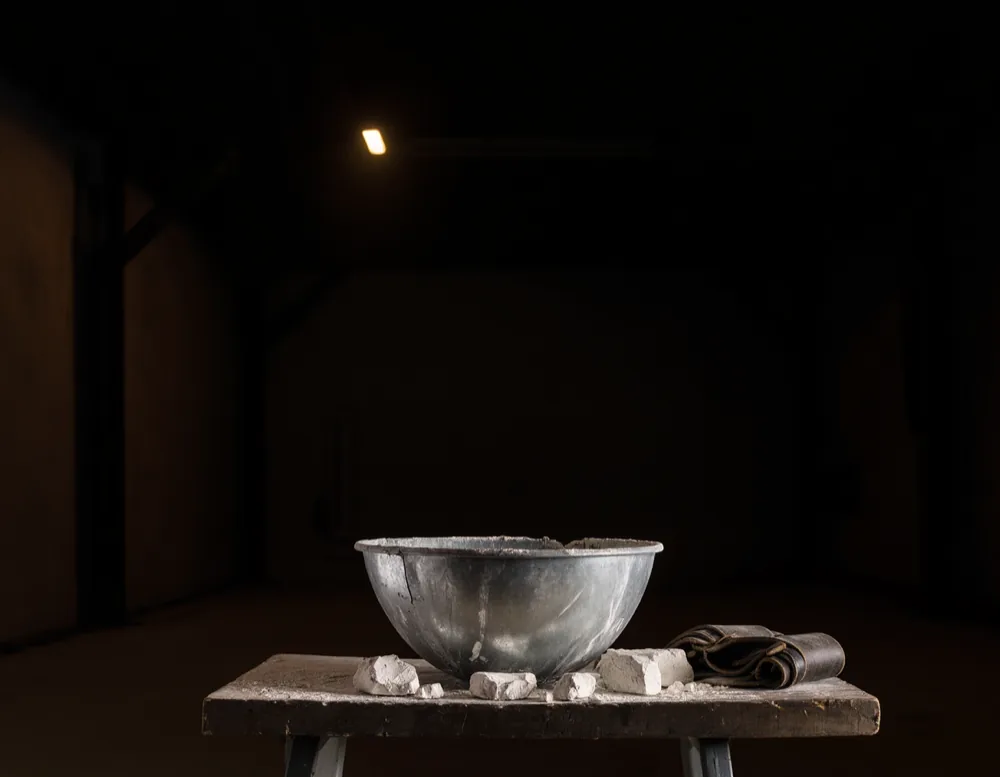 Steel bowl of lifting chalk, a rolled belt and knee sleeves on a worn wooden bench